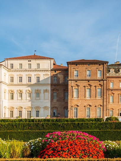 Baroque palace facade with colorful garden in Venaria Reale, Italy.