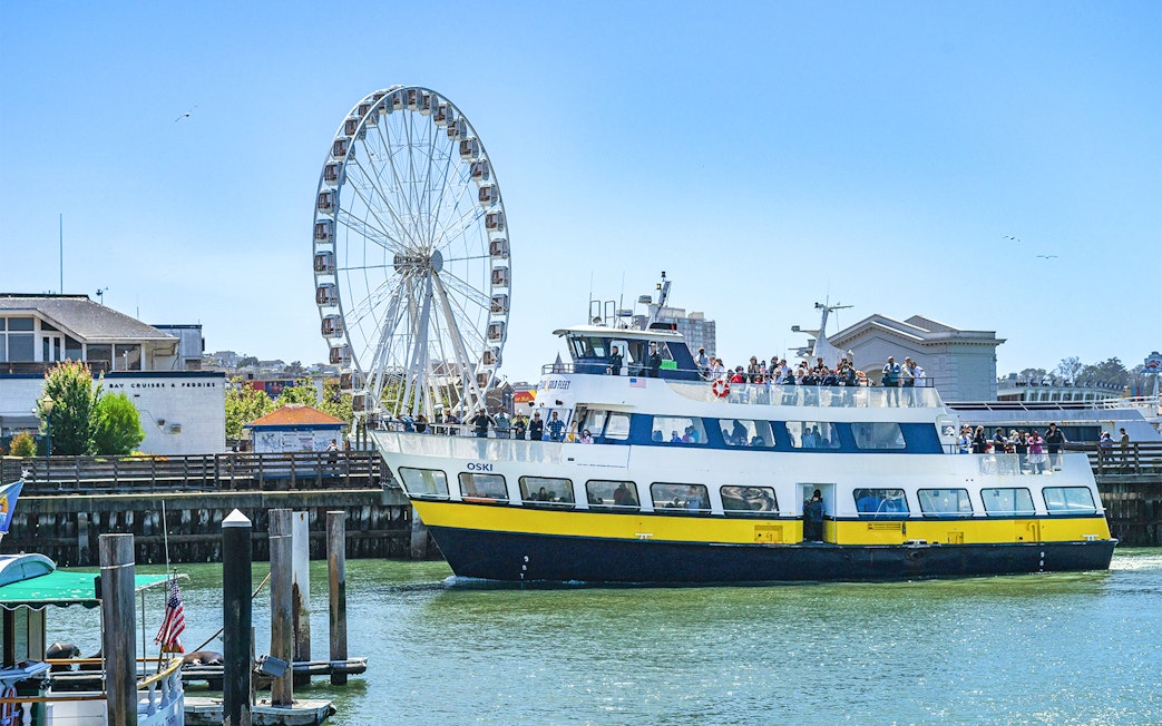 Ferry near San Francisco coast with Ferris wheel in background.