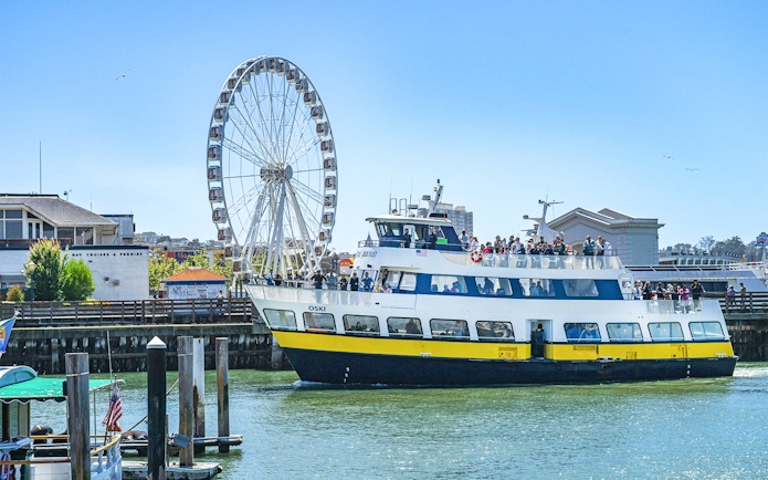 Ferry near San Francisco coast with Ferris wheel in background.