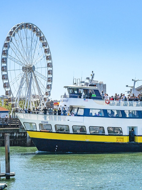 Ferry near San Francisco coast with Ferris wheel in background.