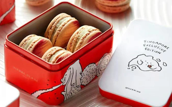 Red tin box of Pierre Hermé macarons with Singapore-themed lid illustration.