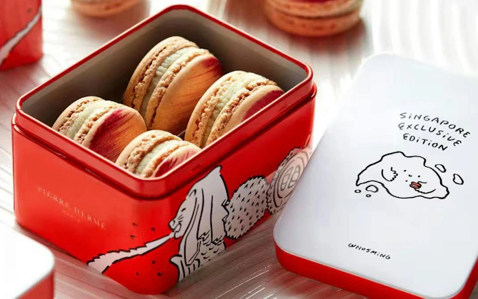 Red tin box of Pierre Hermé macarons with Singapore-themed lid illustration.