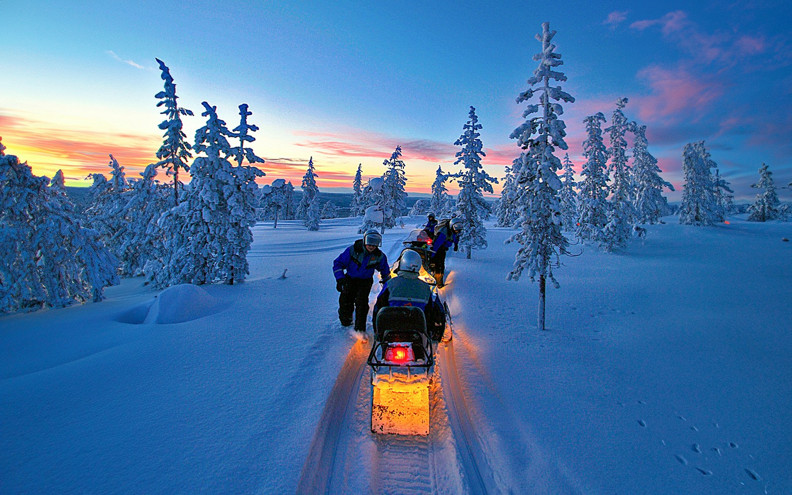 Snowmobiles on snowy trail under Northern Lights in Rovaniemi, Finland.
