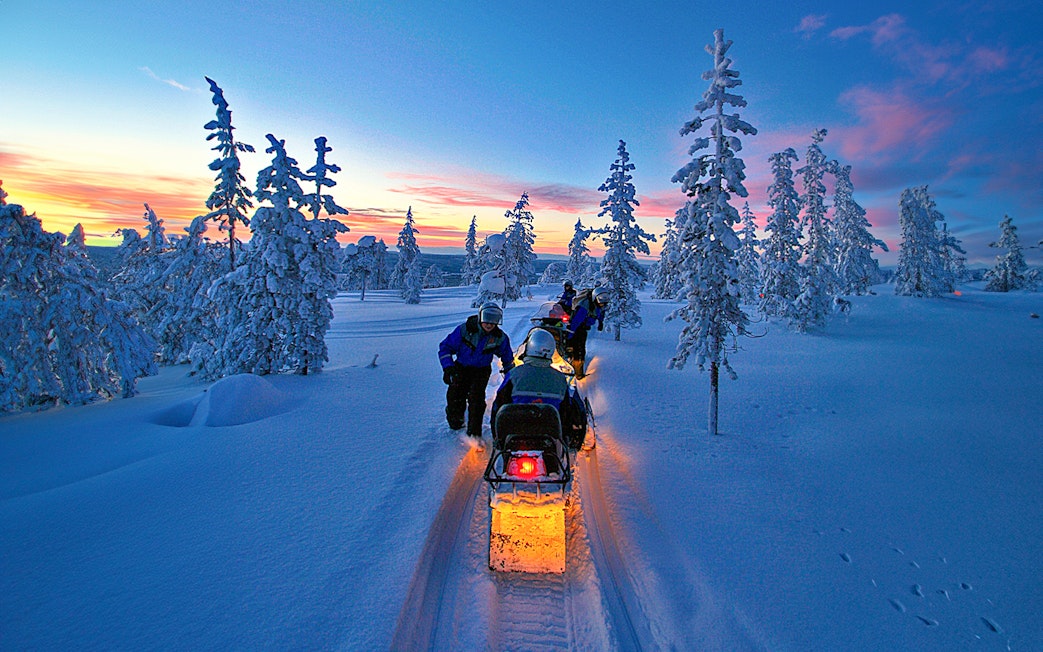 Snowmobiles on snowy trail under Northern Lights in Rovaniemi, Finland.