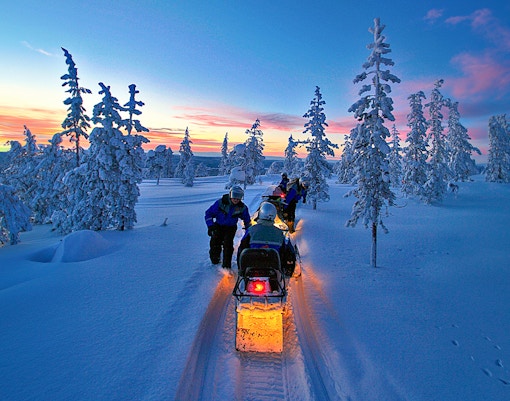 Snowmobiles on snowy trail under Northern Lights in Rovaniemi, Finland.