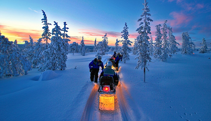 Snowmobiles on snowy trail under Northern Lights in Rovaniemi, Finland.