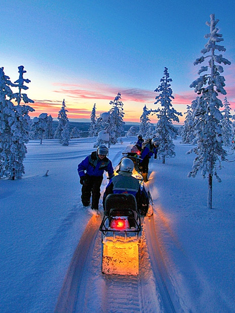 Snowmobiles on snowy trail under Northern Lights in Rovaniemi, Finland.