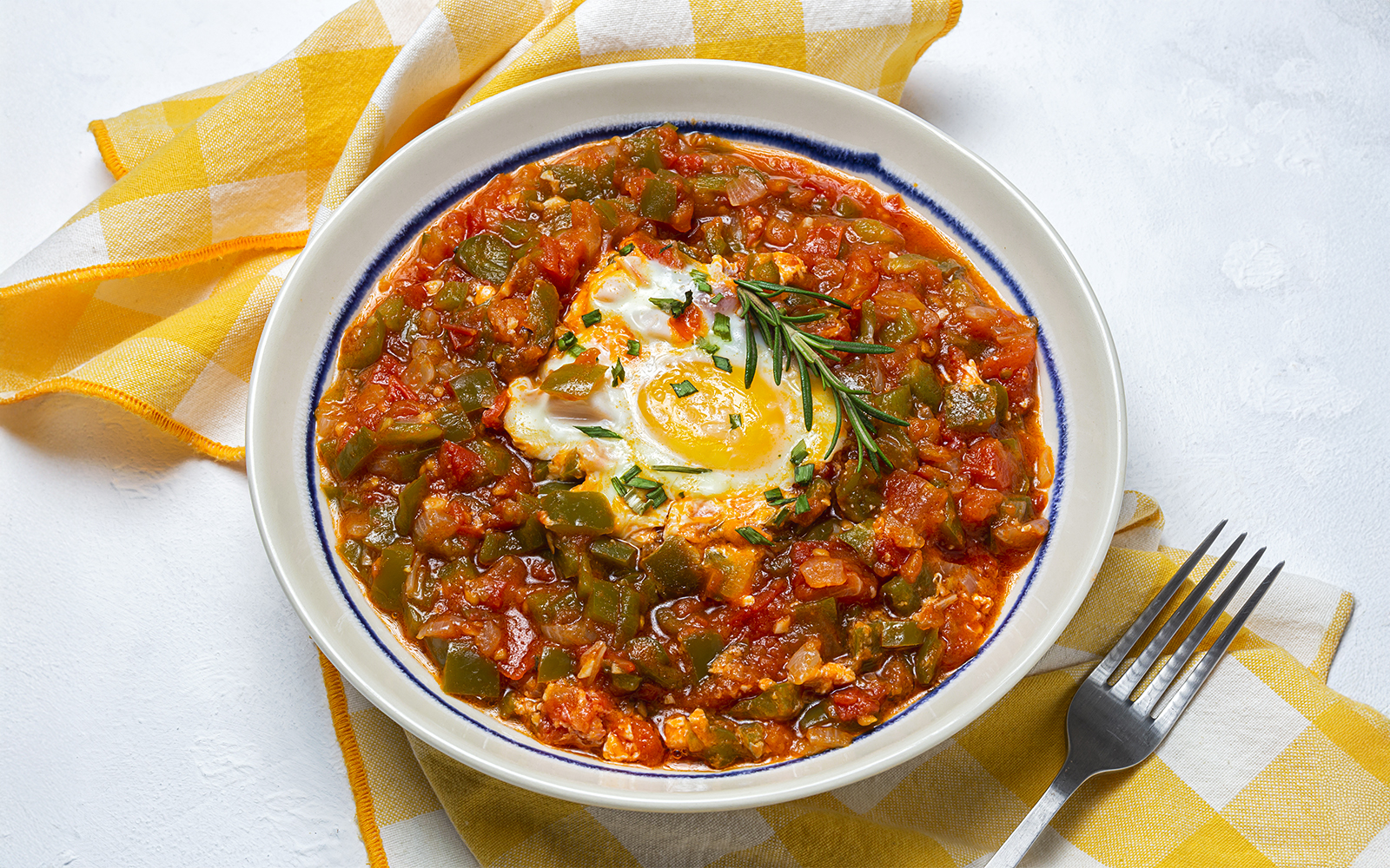 Ratatouille with manchego cheese and egg, garnished with rosemary, on a white plate.