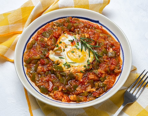 Ratatouille with manchego cheese and egg, garnished with rosemary, on a white plate.