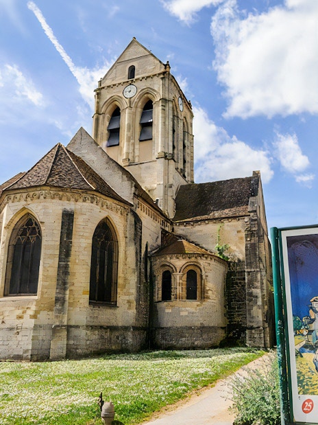 Gothic church in Giverny with a sign displaying Monet's painting, part of a guided tour from Paris.