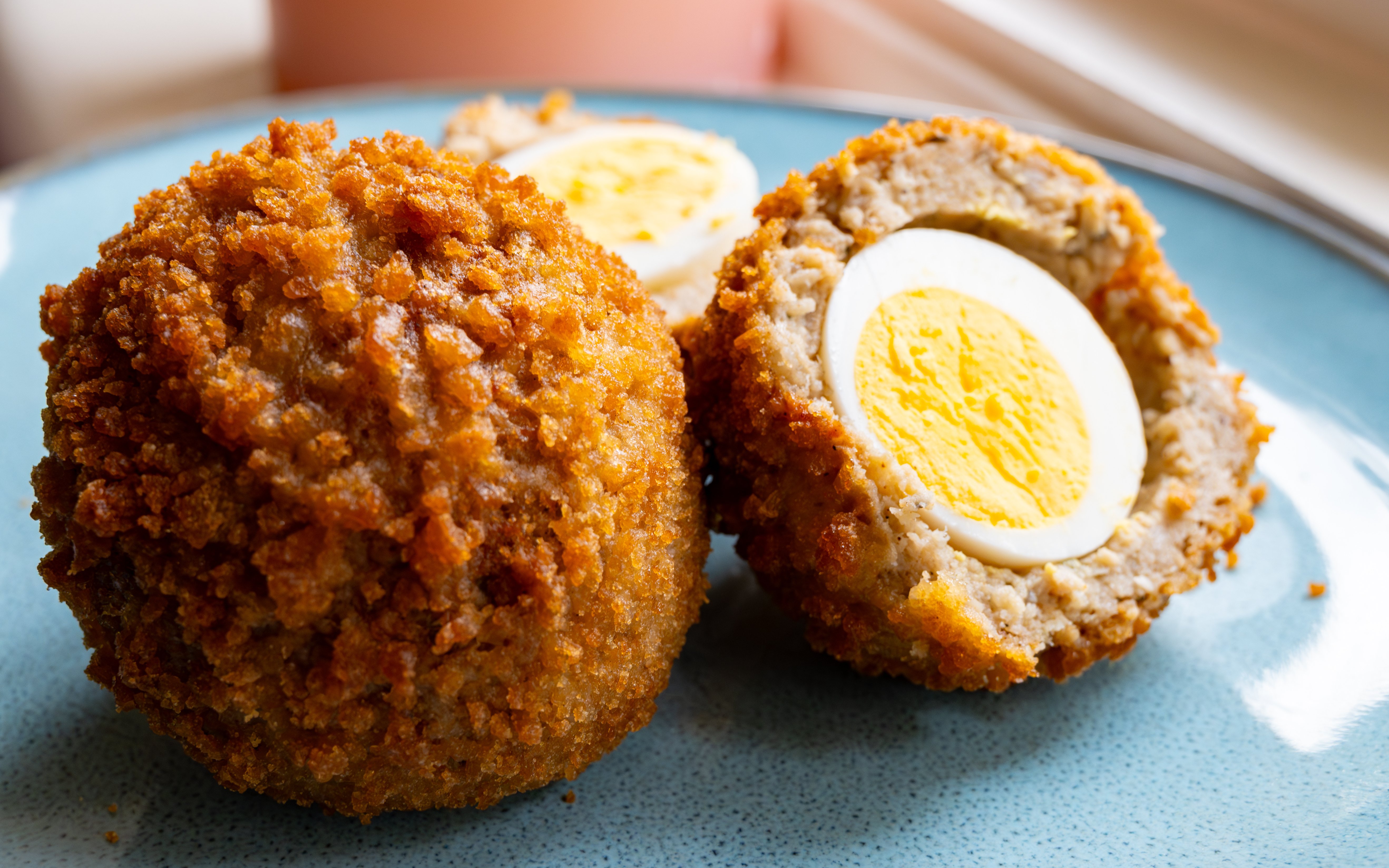 Stuffed Scotch eggs with panko breadcrumbs on a blue plate.