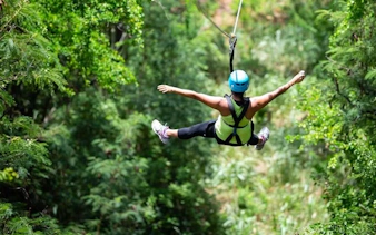 Person ziplining through lush forest with modern braking system.