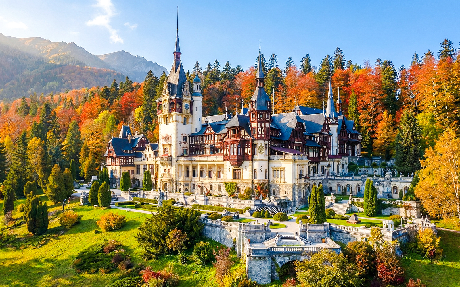 Peleș Castle in Romania surrounded by autumn trees and mountains.