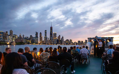 Nighttime Chicago River cruise with skyline view and passengers on deck.