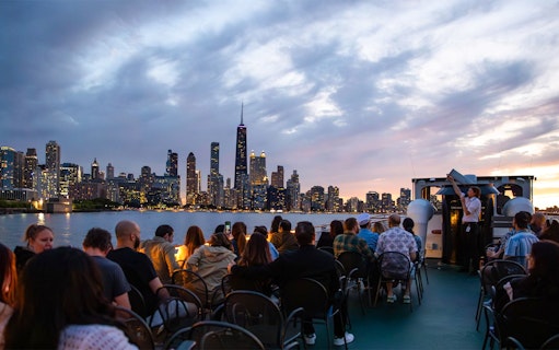 Nighttime Chicago River cruise with skyline view and passengers on deck.