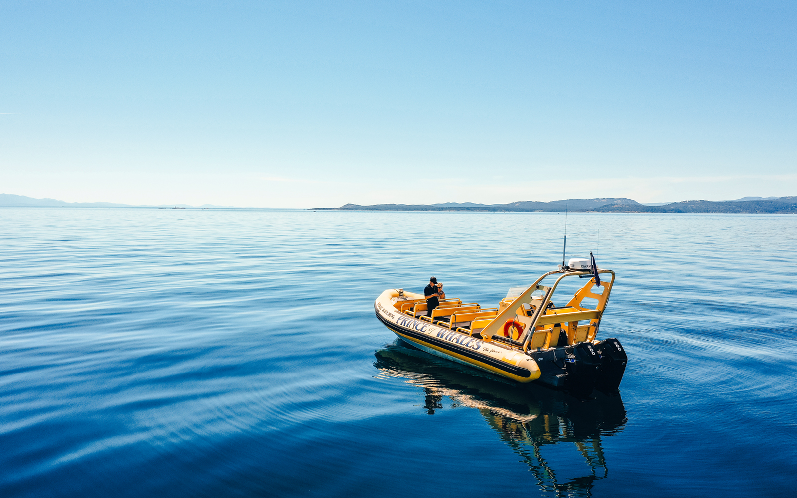 Yellow inflatable boat on calm blue sea, used for whale watching tours.