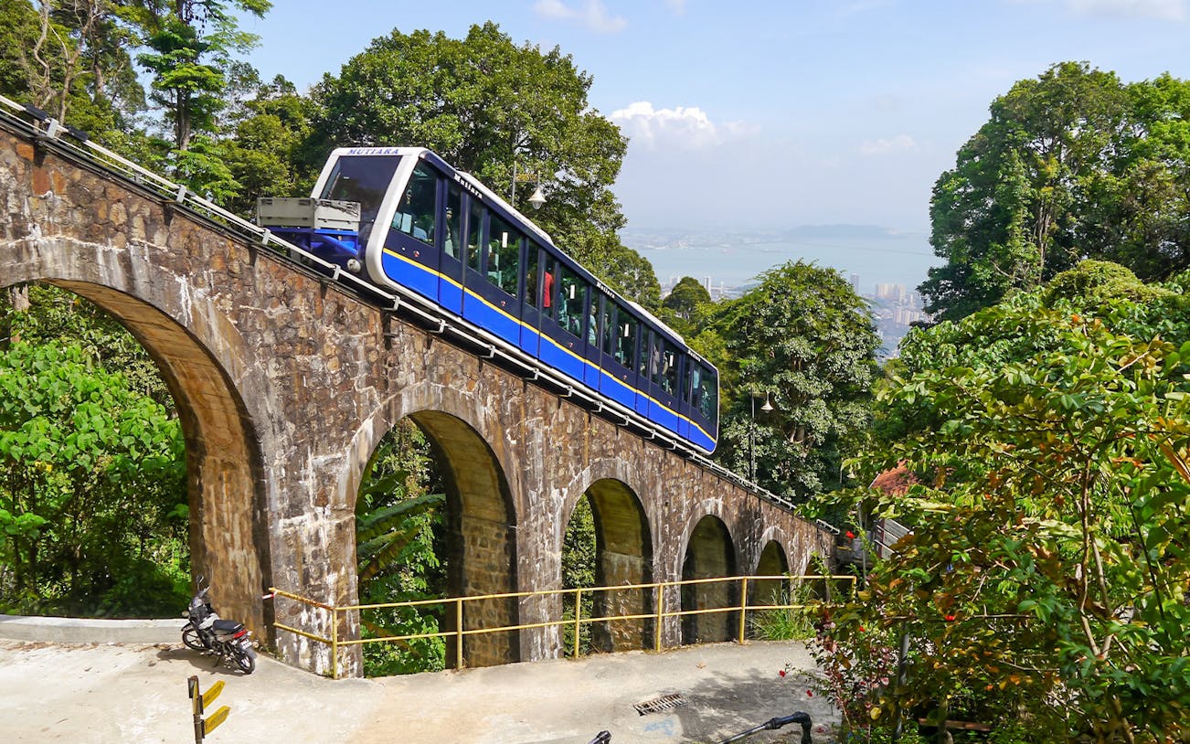 Funicular train ascending Penang Hill, Malaysia, with lush greenery and city view.