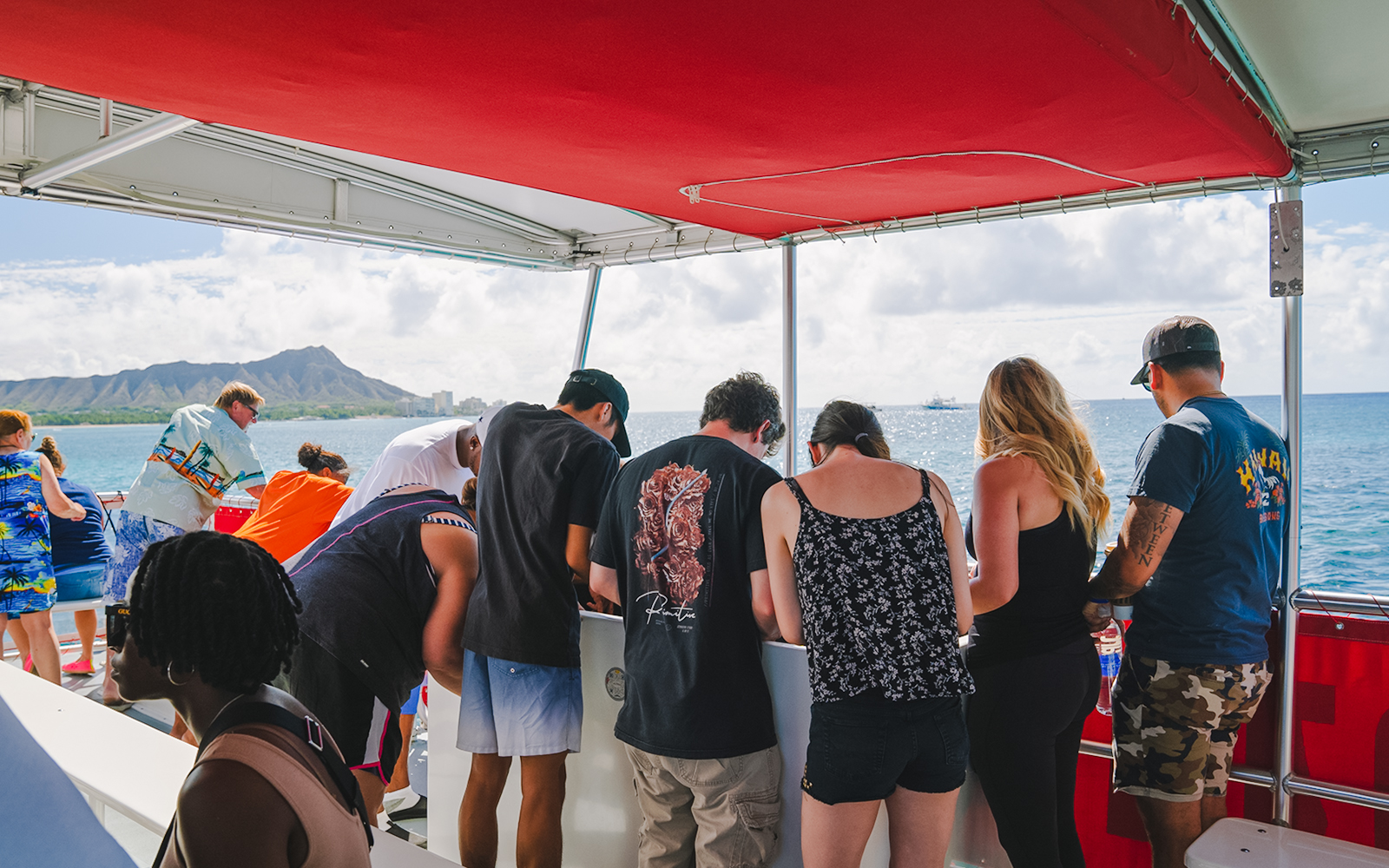Guests observing marine life on a Hawaii glass-bottom boat tour with Diamond Head in the background.