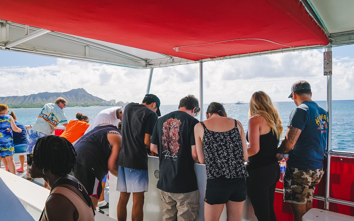 Guests observing marine life on a Hawaii glass-bottom boat tour with Diamond Head in the background.