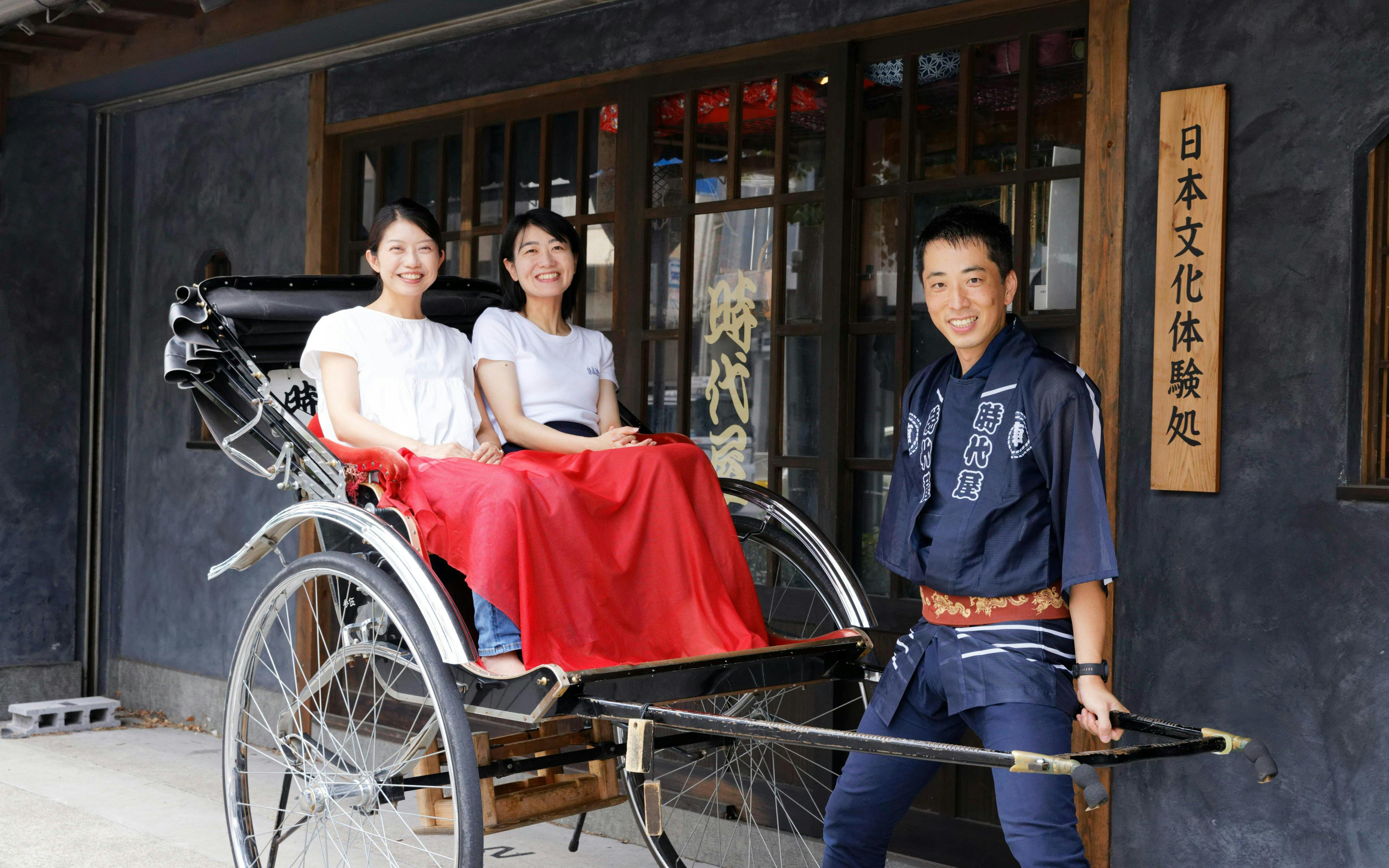 Two women seated in a rickshaw with a guide in Asakusa, Tokyo.