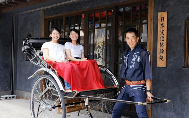 Two women seated in a rickshaw with a guide in Asakusa, Tokyo.