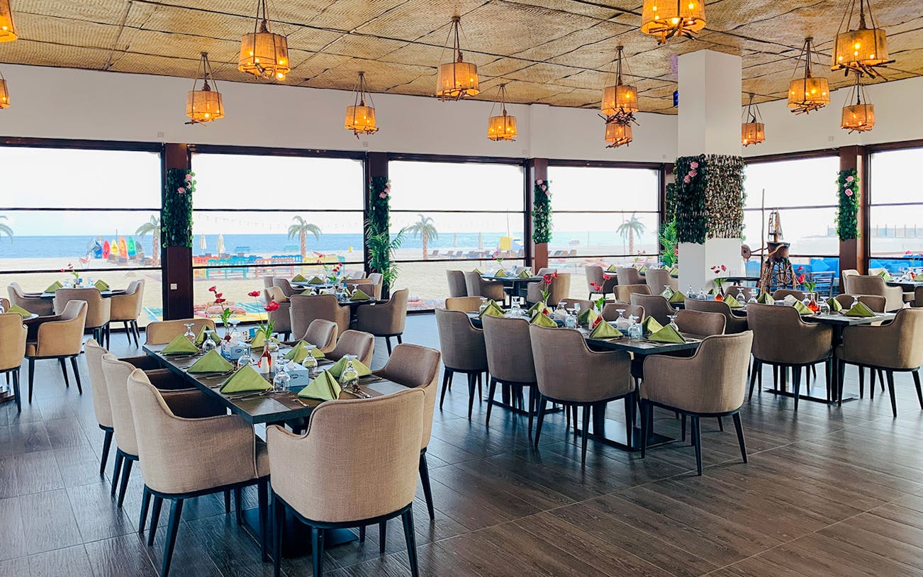 Dining area with ocean view at Al Majles Resort, featuring set tables and hanging lights.