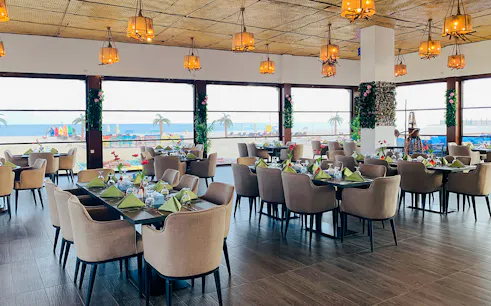 Dining area with ocean view at Al Majles Resort, featuring set tables and hanging lights.