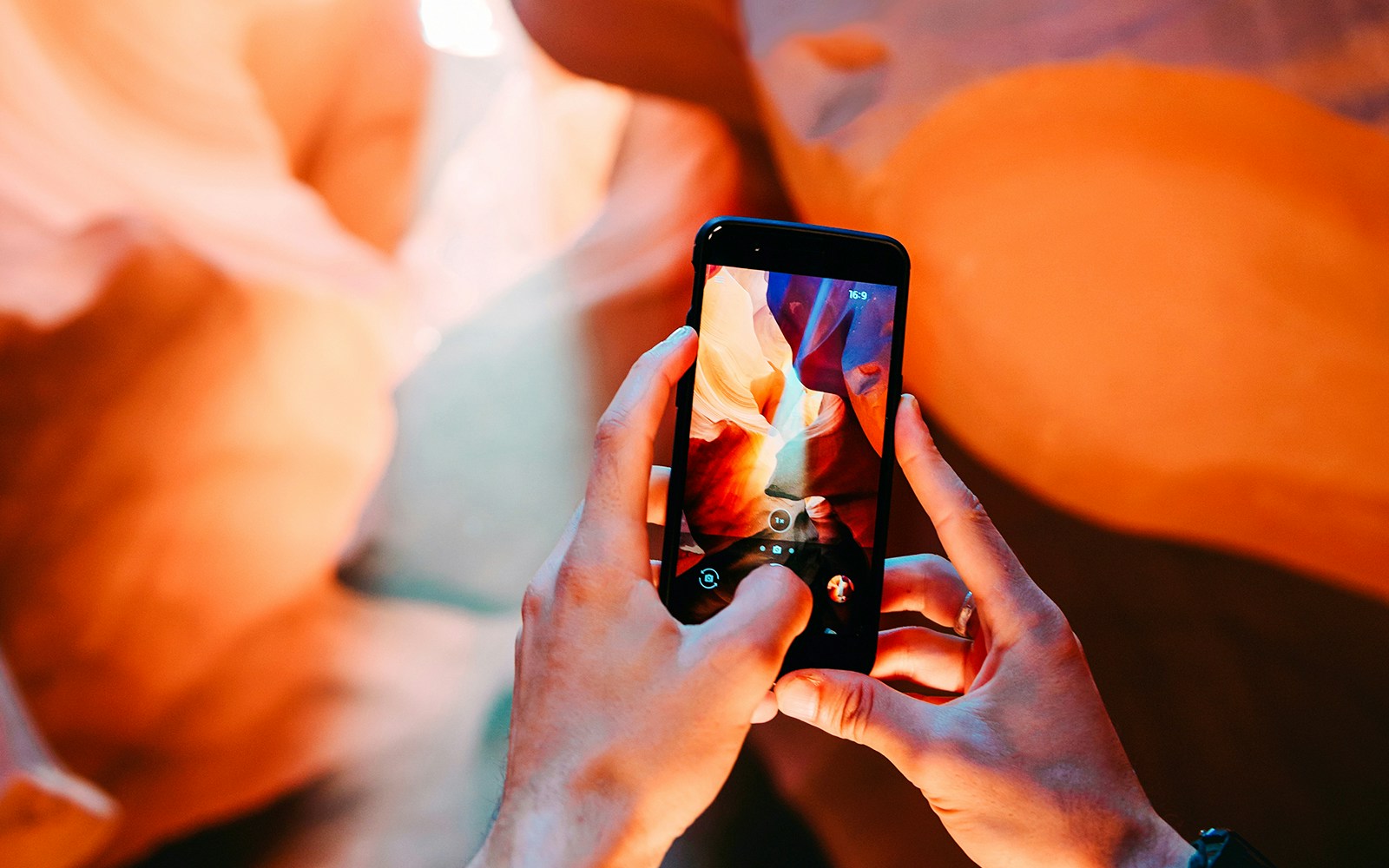 Man photographing Antelope Canyon's rock formations with smartphone.