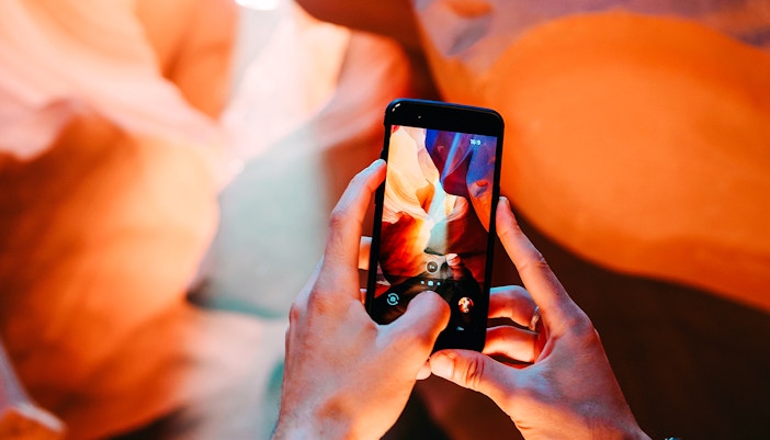 Man photographing Antelope Canyon's rock formations with smartphone.