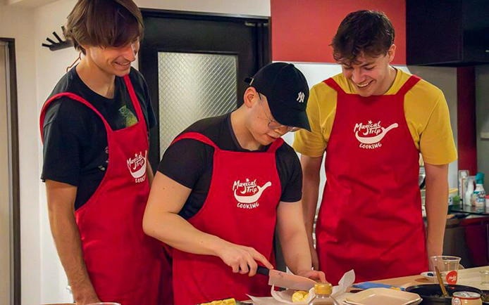 Participants in red aprons preparing ingredients during a Tokyo izakaya-style cooking class.