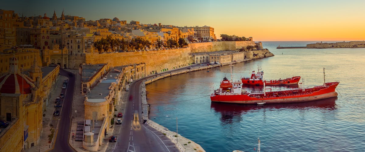 Great Harbour in Malta with a red ship docked at sunset.