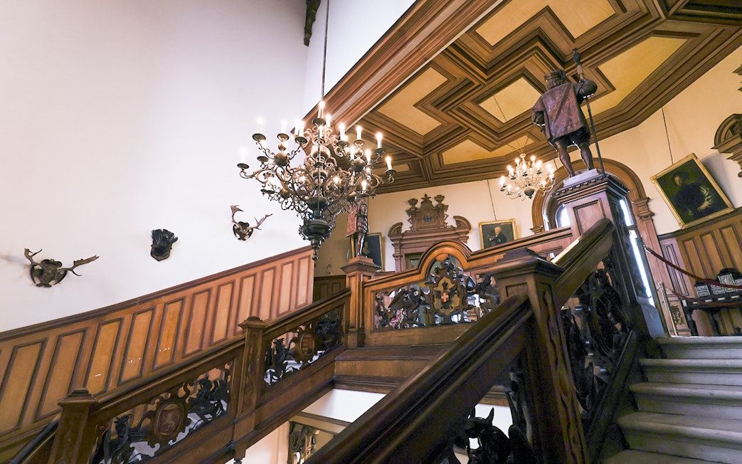 Miramare Castle staircase with ornate woodwork and chandeliers leading to the upper floor.