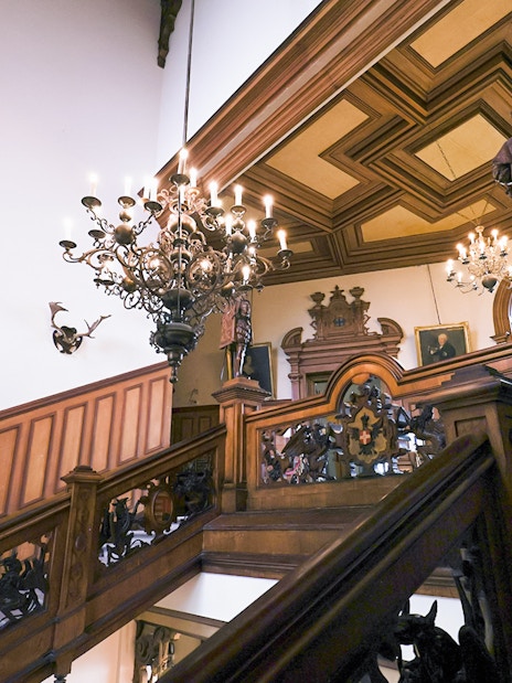 Miramare Castle staircase with ornate woodwork and chandeliers leading to the upper floor.