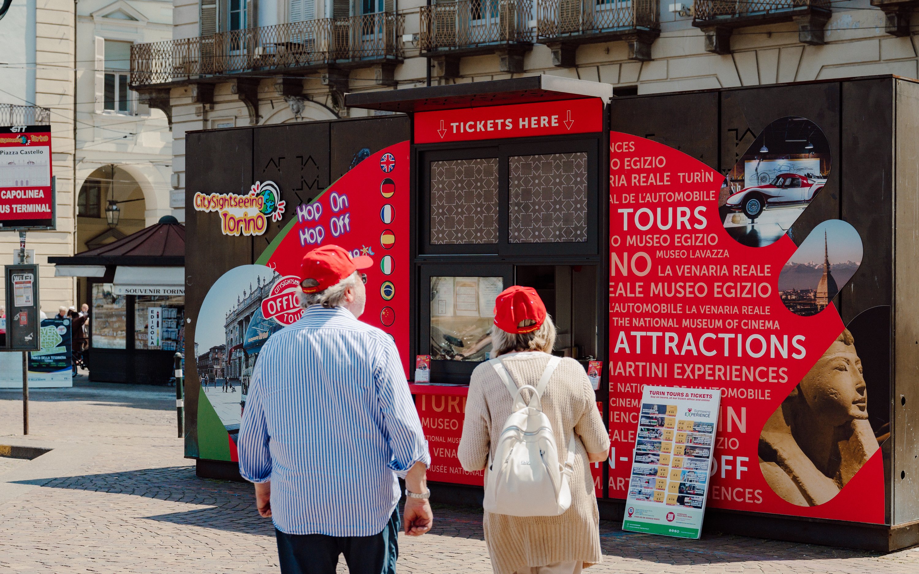 Tourists at City Sightseeing Turin Hop-on Hop-off bus ticket booth in Piazza Castello.