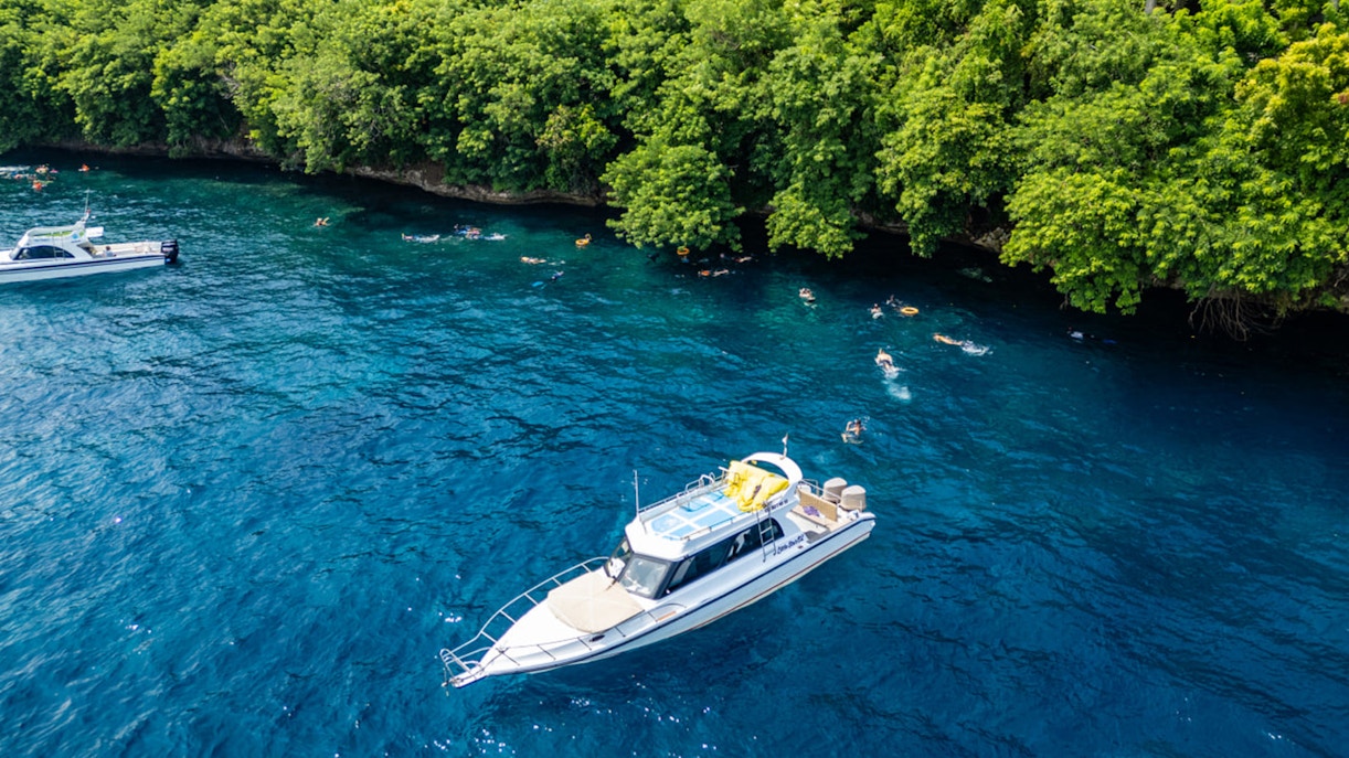 Tourists snorkeling near boats at Nusa Penida, exploring coral reefs and marine life in Bali.