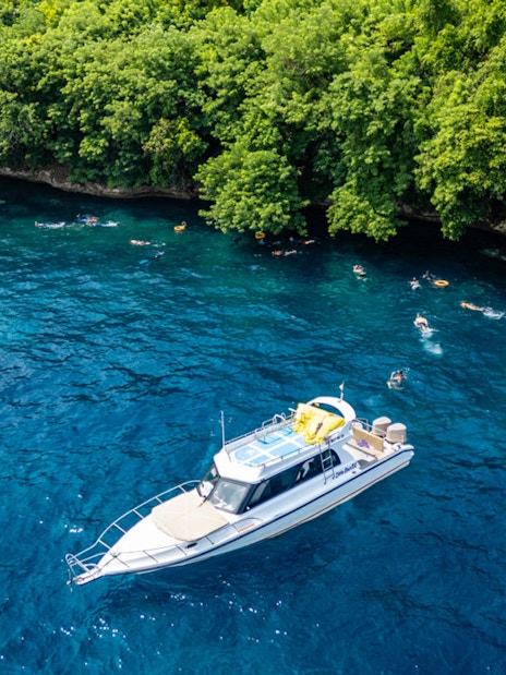 Tourists snorkeling near boats at Nusa Penida, exploring coral reefs and marine life in Bali.