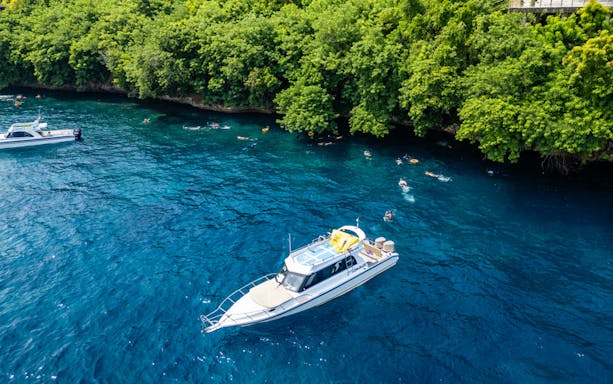 Tourists snorkeling near boats at Nusa Penida, exploring coral reefs and marine life in Bali.