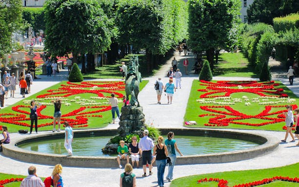Visitors walking through Mirabell Gardens with vibrant flower beds in Salzburg, Austria.