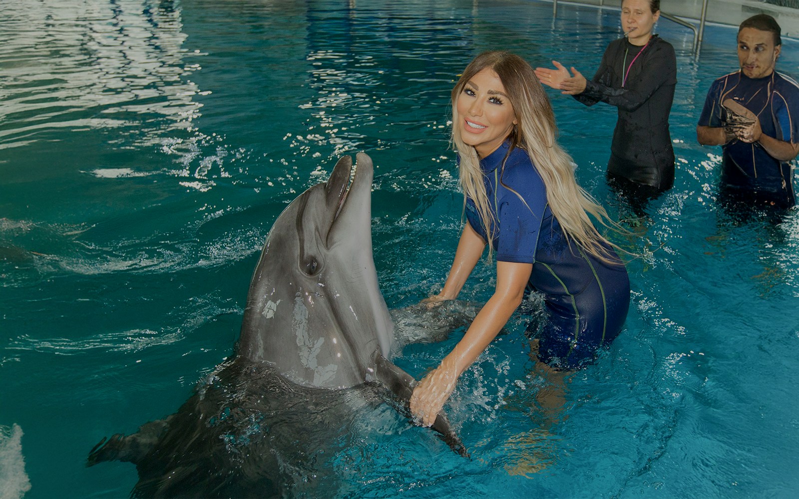 A girl interacting with a dolphin and posing for a picture