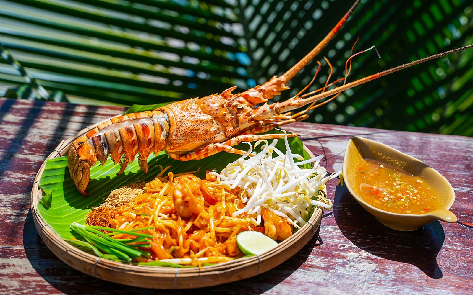 Pad Thai with lobster, bean sprouts, and sauce on a banana leaf plate.