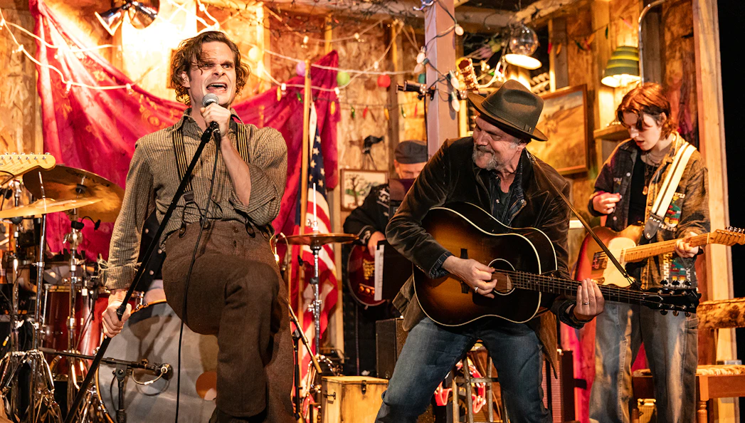Band performing lively music on stage with a singer and guitarists, themed around Dead Outlaw.