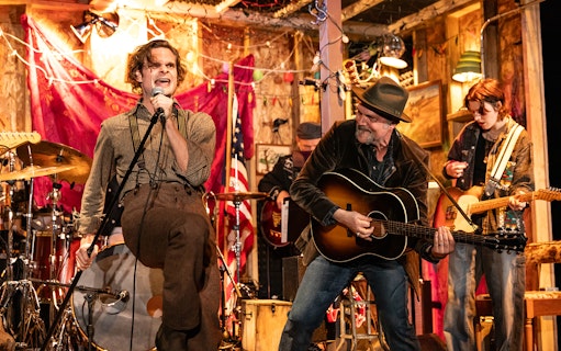 Band performing lively music on stage with a singer and guitarists, themed around Dead Outlaw.