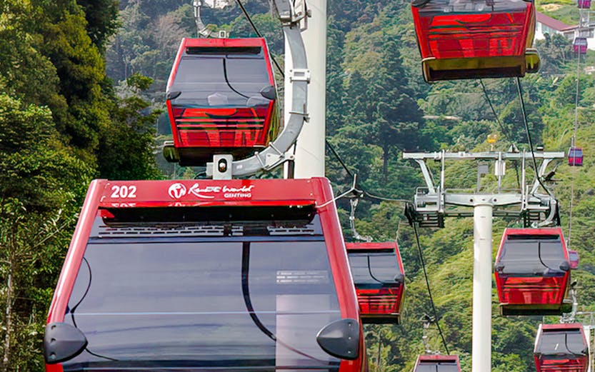 Red cable cars of Awana Skyway ascending through lush forest in Genting Highlands, Malaysia.