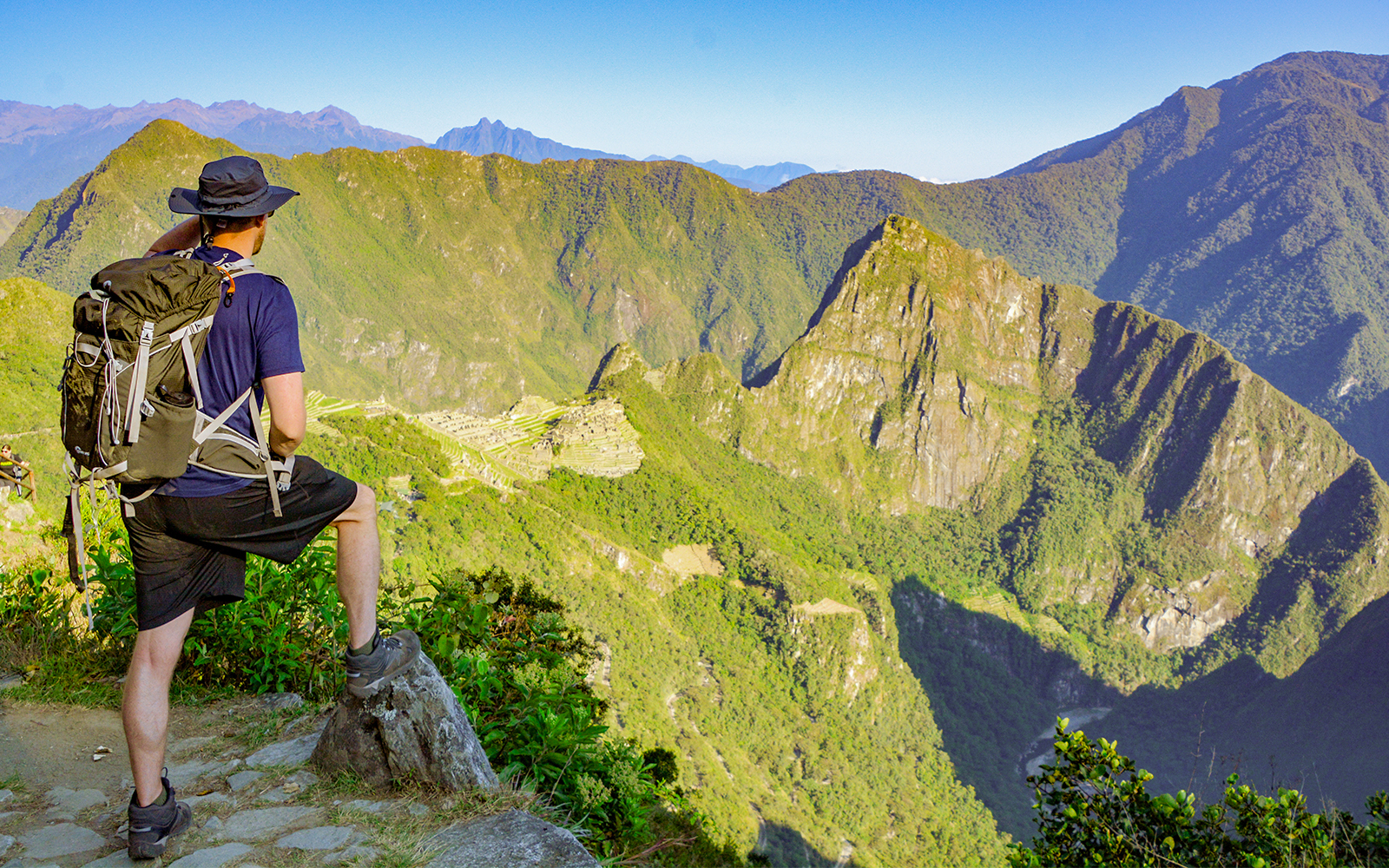 Hiker overlooking Machu Picchu ruins in Peru with surrounding mountains.