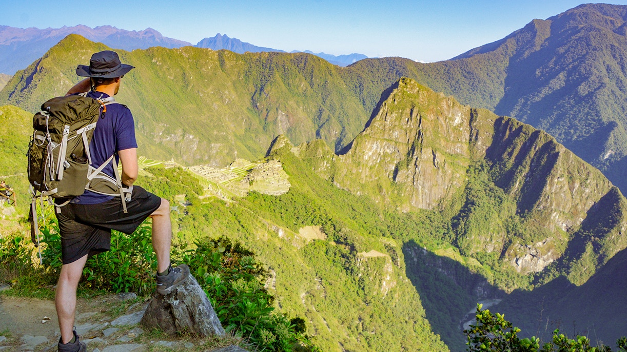Hiker overlooking Machu Picchu ruins in Peru with surrounding mountains.