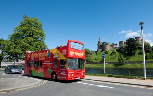 Open-top tour bus near Inverness Castle on a sunny day.