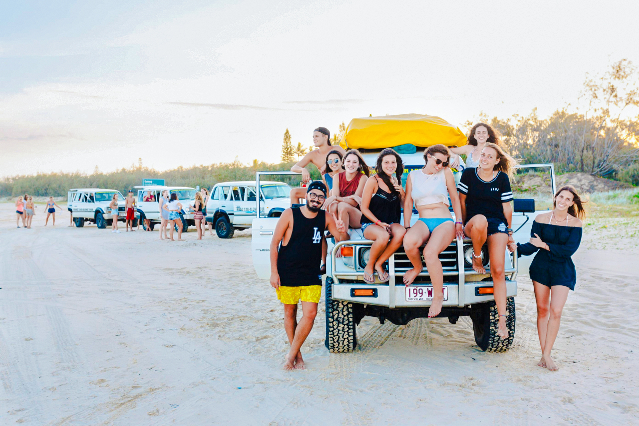 Tourists sitting on a 4WD vehicle on Fraser Island beach, K'gari drive experience.