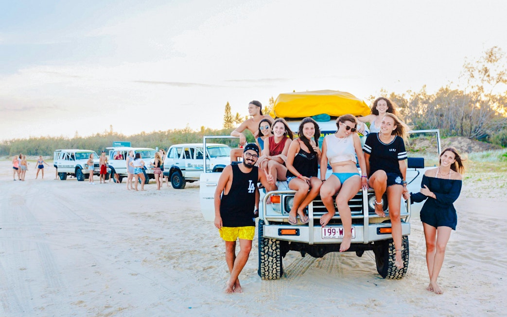 Tourists sitting on a 4WD vehicle on Fraser Island beach, K'gari drive experience.
