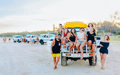 Tourists sitting on a 4WD vehicle on Fraser Island beach, K'gari drive experience.