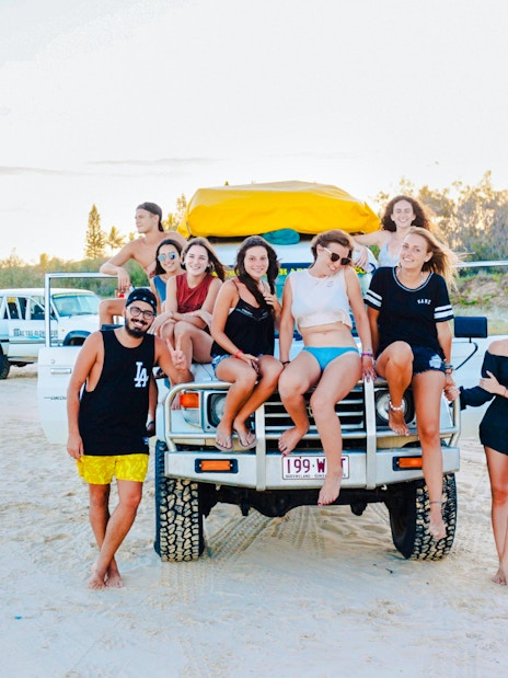 Tourists sitting on a 4WD vehicle on Fraser Island beach, K'gari drive experience.